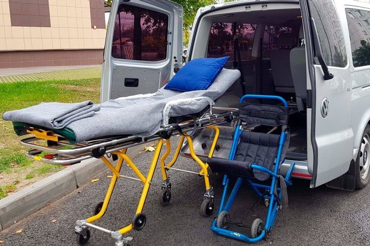 Stretcher with blankets and a folding transport wheelchair set out behind the open rear doors of a transport van